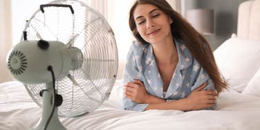 smiling woman laying in bed with fan blowing in her face