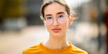serious woman wearing glasses standing outside thinking