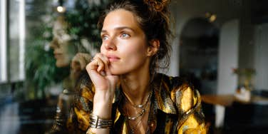 A woman bathed in soft morning light looks out a window with quiet strength, capturing the bittersweet beauty of learning what real love feels like beyond the fairy tale.