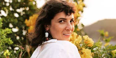 Woman in soft light looking over her shoulder with a gentle smile, reflecting the calm confidence and self-forgiving habits practiced by people skilled in self-compassion.