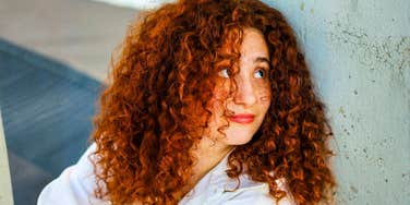 Confident, composed woman with red curly hair outdoors showing the art of emotional command and habits of people who stay present in tough times.