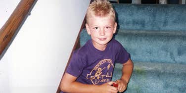 Young 90s kid sitting, playing on blue carpeted stairs, capturing the forgotten life lessons that shaped stronger generations.
