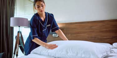 young female housekeeper at hotel making bed