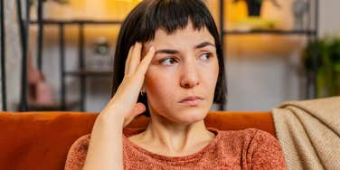 Upset woman with hand in her hair, deep in thought about her relationship, reflecting the painful truth of loving the idea of someone, not the person.