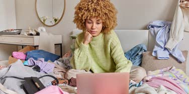 woman sitting on bed surrounded by clutter and mess