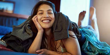 smiling woman sitting in unmade bed with laundry everywhere