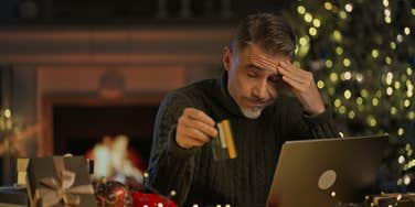 stressed man buying gifts for the holidays on his laptop holding credit card