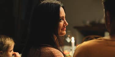 Woman looking knowingly at partner while family is gathered around a Thanksgiving table showing how certain phrases can instantly change the holiday vibe.