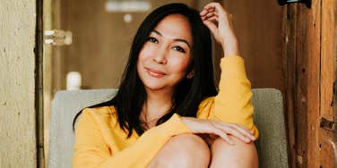 Woman sitting comfortably indoors with a soft, relaxed smile and calm posture, embodying the art of being unbothered and the simple ways to stay happy even when life feels like a chore.