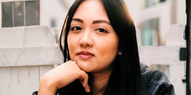 Thoughtful woman resting her chin on her hand with a calm, self-aware expression, reflecting the art of doing better and the simple ways to stop doing the things you know aren’t helping.