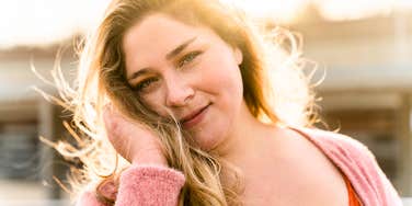 Confident woman smiling softly in warm sunlight showing the art of self-worth and the habits of people who don’t need anyone to confirm their greatness.