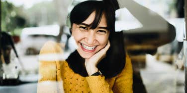 Woman smiling softly through a window with relaxed, genuine warmth, illustrating the subtle charm that helps people build instant goodwill with others.