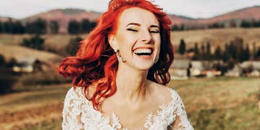 Laughing bride in a lace wedding dress outdoors, appearing relaxed and genuinely happy.