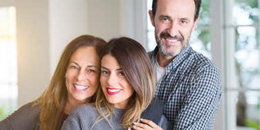 mother and father hugging adult daughter happy family