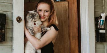 smiling young woman holding cat at her front door