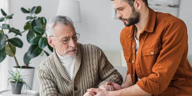 older father holding adult son's hands looking worried