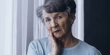sad lonely older woman waiting by the window curtains