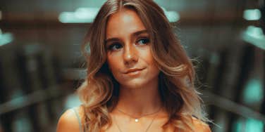 Thoughtful person with soft expression looking slightly to the side in a dimly lit indoor space, appearing introspective and calm.