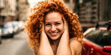 Joyful woman laughing with her hands in her hair on a city street, capturing the hopeful moment when you know life is about to get good and new kinds of problems start to appear.