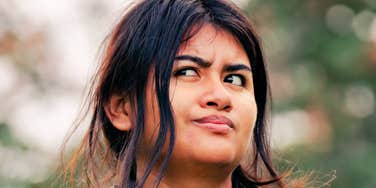 Woman outdoors glancing sideways with a skeptical, calculating expression, as if quietly reassessing a relationship dynamic.