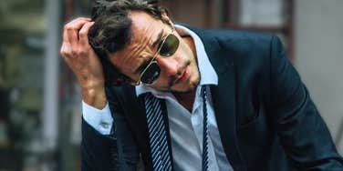 Distant man in a suit looking overwhelmed and disconnected, illustrating the telltale behaviors of men who will never be your person no matter how hard you love them.