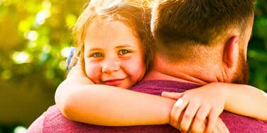 Smiling child hugging an adult’s shoulders outdoors, representing an article about parenting habits that raise genuinely good humans