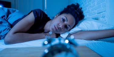 tired woman looking at clock as she stays up late
