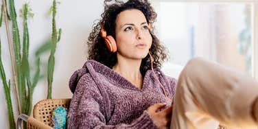 Woman sitting indoors listening to music and thinking, representing people who wonder whether certain thoughts or habits could be OCD, as an OCD specialist explains what OCD actually is.