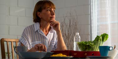sad older woman eating meal alone at dinner table