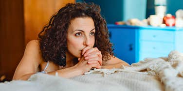 Woman next to a bed with clasped hands, representing personality traits of people who don’t make their bed every morning