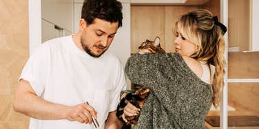 Couple navigating a playful, chaotic kitchen moment with a cat showing the real-life cat-and-dog messiness behind how partners fight fair.