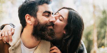Man and woman standing outdoors in a wooded area, sharing a quiet moment together.