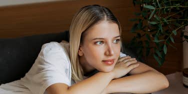 Woman resting on a couch with her arms folded, looking outward in a calm, quiet moment.