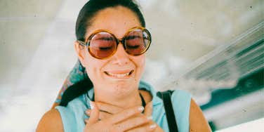 Woman wearing sunglasses giving a polite smile that suggests discomfort or awkwardness.