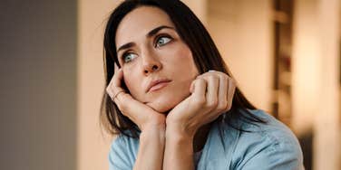 Thoughtful woman resting her face in her hands, looking off to the side as she reflects on how to ease tension in a difficult family relationship.