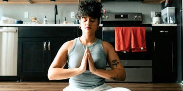 Woman sitting in quiet meditation with hands pressed together, capturing the ancient practice of spiritual alignment that brings body and mind back into balance.