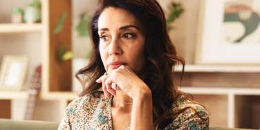 Thoughtful middle-aged woman sitting at home, appearing reflective and calm while thinking quietly.