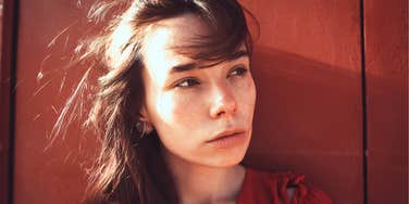 Woman with freckles looking off to the side in quiet reflection, appearing thoughtful and emotionally guarded.