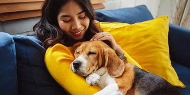 woman cuddling with sleeping dog on couch at home