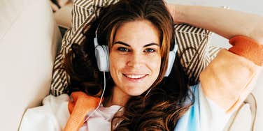 A woman relaxing on a couch with headphones on, smiling comfortably indoors.