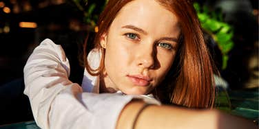 A woman gazes calmly toward the camera while extending her arm, conveying quiet boundaries and emotional distance.