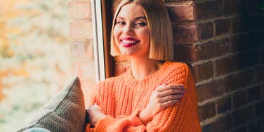 complex thinking woman with high-level traits smiling in windowsill
