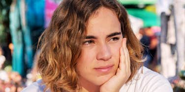 Woman resting her face in her hand outdoors, looking thoughtful in natural light.