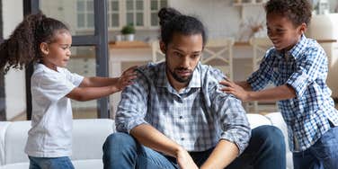 frustrated dad sitting on couch ignoring kids wanting to play