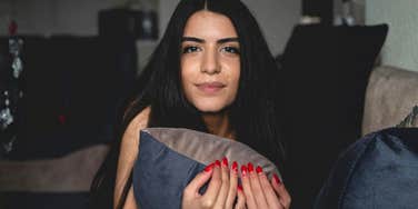 Woman sitting on a couch holding a pillow, looking calm but guarded, reflecting emotional self-protection after a painful breakup