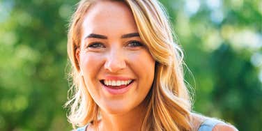 A smiling woman outdoors with greenery in the background.
