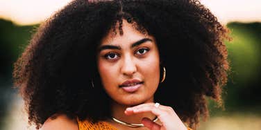 Confident woman with natural curly hair looking directly at the camera outdoors, conveying self-assurance and emotional steadiness