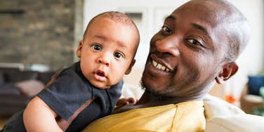Parent holding a baby and smiling indoors.