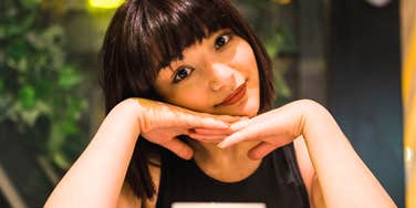 Woman resting her chin on her hands while sitting at a table with a cup.