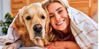 woman smiling laying next to her happy dog in bed
